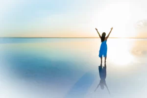 Person standing with arms raised at sunrise expressing gratitude and positivity